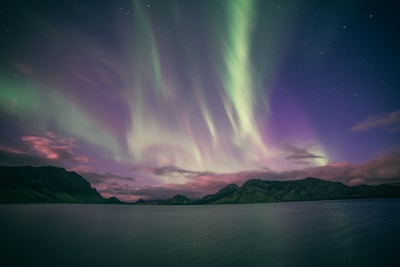 A family gazing up at a vibrant aurora borealis over a serene mountain lake at dusk.