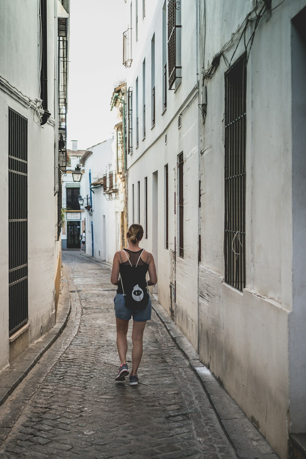 woman in blue tank top and blue denim shorts walking on sidewalk during daytime