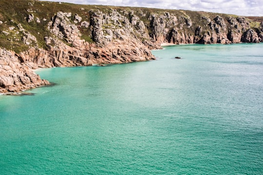 wide angle photo of cliff near body of water in Porthcurno Beach United Kingdom