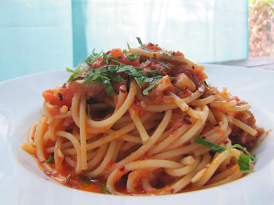 Close-up of handmade pasta tossed in a rich tomato sauce, garnished with fresh basil.