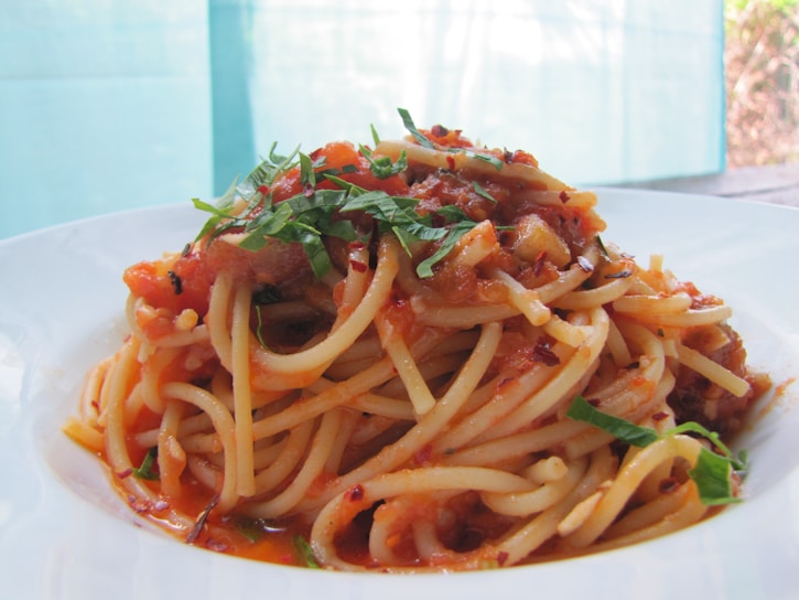 A close-up of a steaming plate of spaghetti with rich tomato sauce and fresh basil leaves.