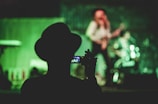 silhouette of man holding camcorder near woman singing on stage