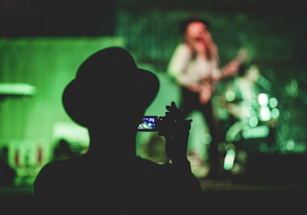 silhouette of man holding camcorder near woman singing on stage