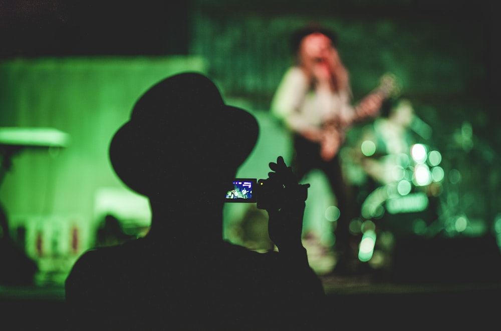 Silueta de hombre sosteniendo videocámara cerca de mujer cantando en el escenario