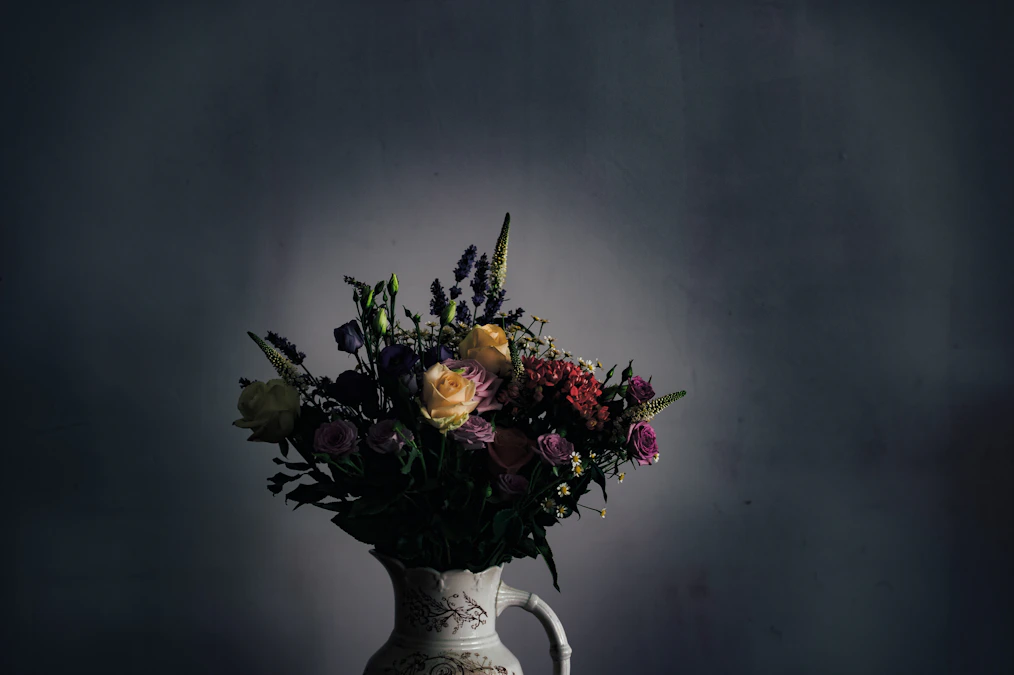 White ceramic vase with assorted flowers against a dark wall