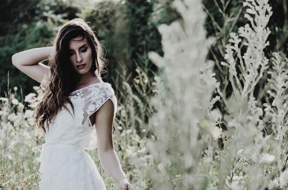 fotografia de foco seletivo da mulher em pé em um campo de flores brancas durante o dia