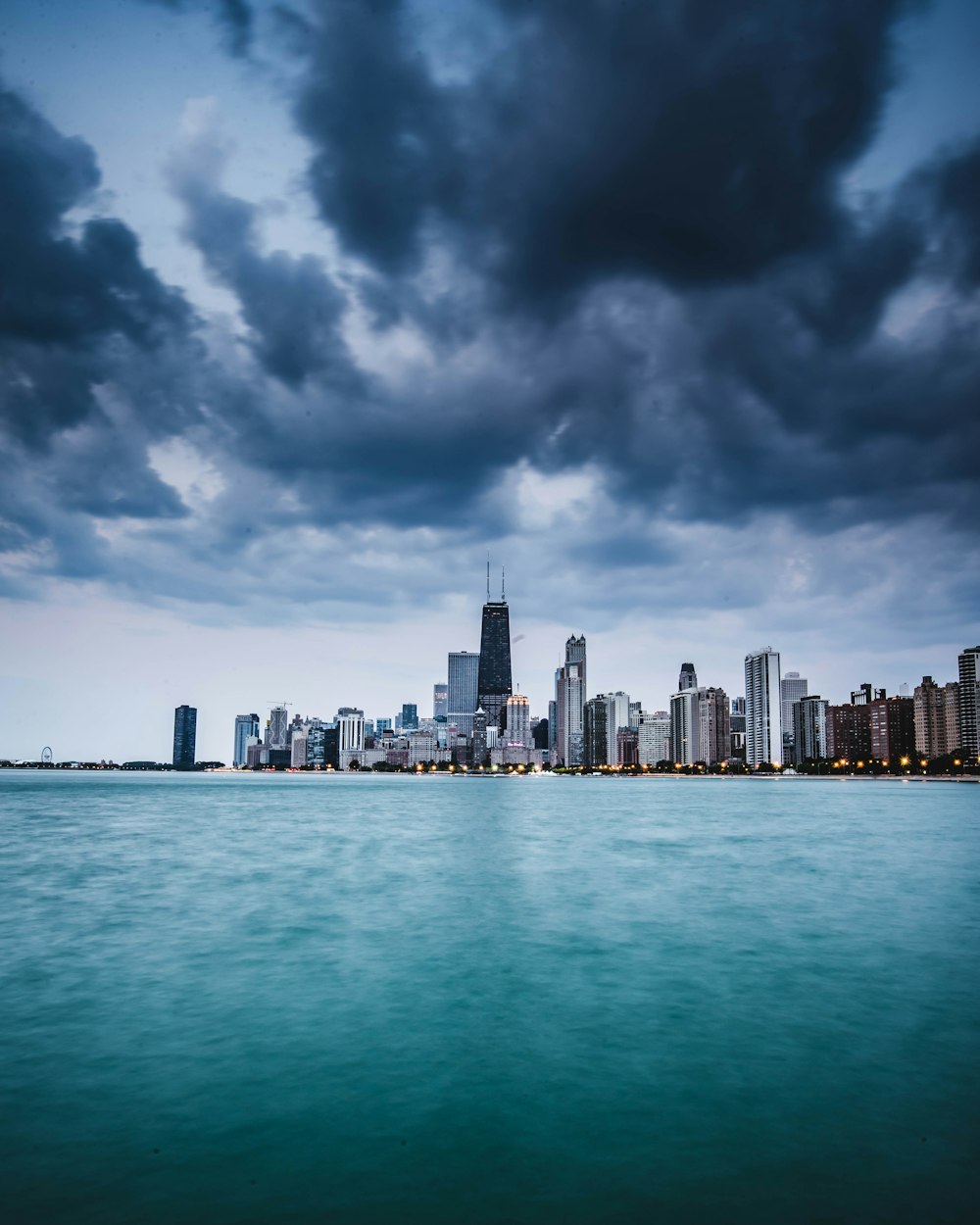 gray and black high-rise buildings beside body of water under gray and white sky at daytime