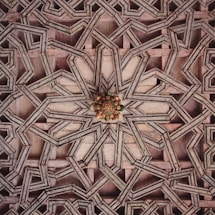 Intricate geometric wooden pattern featuring interlocking star and polygon shapes with a detailed floral motif at the center. The design showcases a layered, three-dimensional effect created by the overlapping wood pieces.