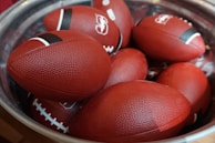 A lineup of footballs with different designs displayed on a wooden shelf.