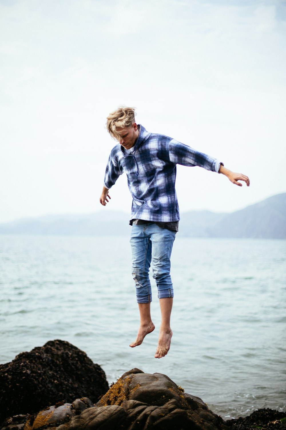 man jumping on rock near body of water