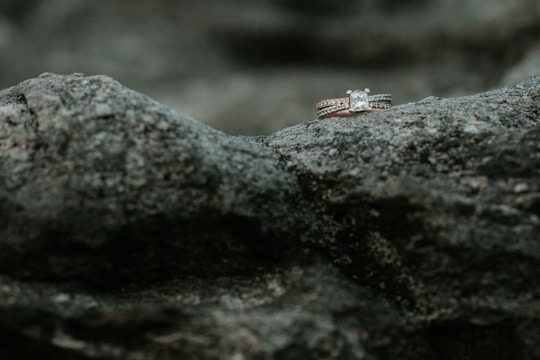 Two diamond rings rest delicately on a rough, textured rock surface, highlighting their sparkle against the muted stone background.