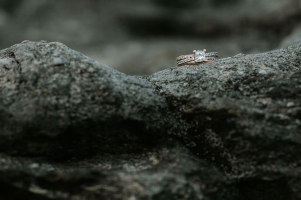Two diamond rings rest delicately on a rough, textured rock surface, highlighting their sparkle against the muted stone background.