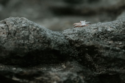 Two diamond rings rest delicately on a rough, textured rock surface, highlighting their sparkle against the muted stone background.