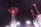 Bright fireworks with red lights and trailing smoke explode against a dark night sky above stadium lights.