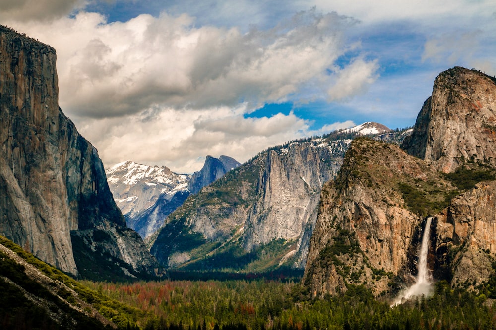 mountain with waterfall under white clouds and blue sky