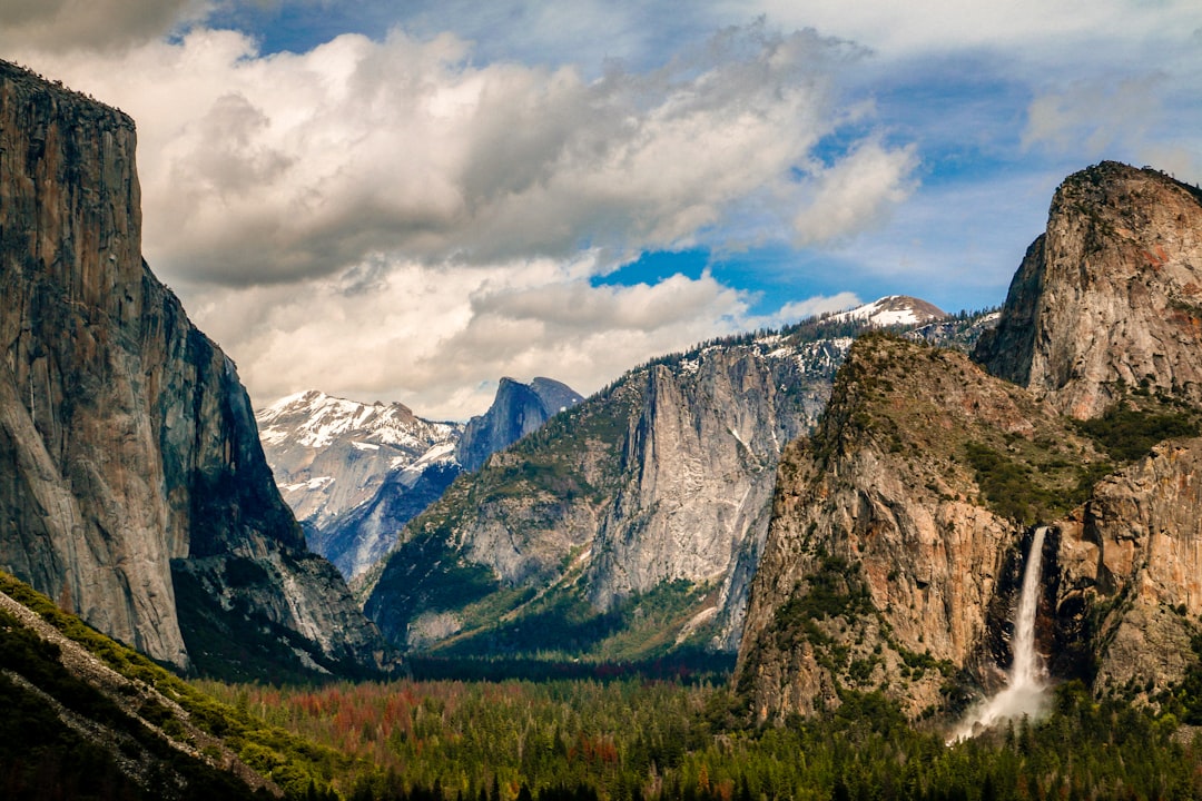 mountain with waterfall under white clouds and blue sky,