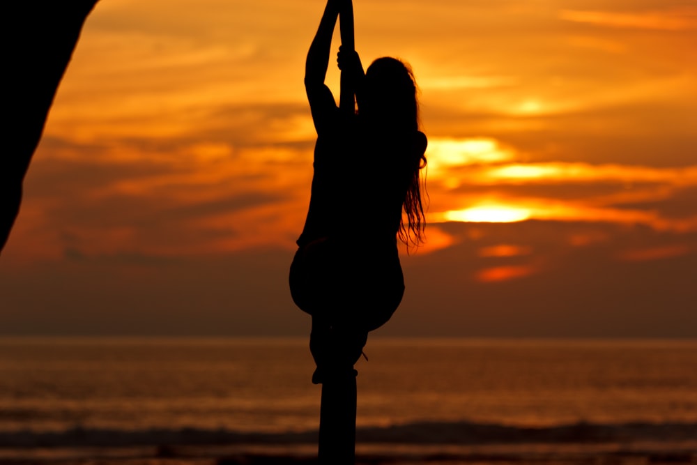 silhouette photo of a man holding rope on seashore during sunset