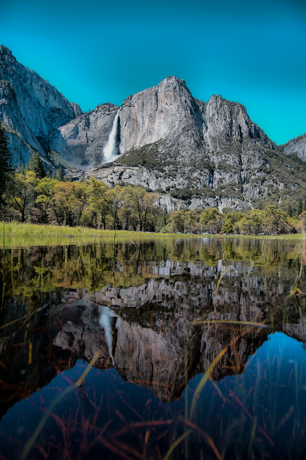 Corpo de água calmo com vista para cachoeiras e montanha de rocha cinza sob o céu azul durante o dia