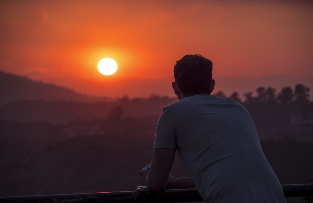 homme portant une chemise bleue regardant le coucher du soleil