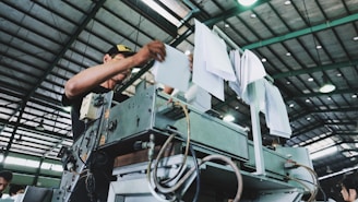 man holding bunch of white papers while operating large gray industrial machine inside well lighted room