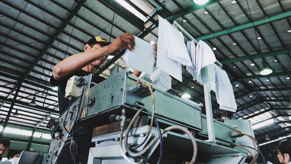 uomo che tiene un mazzo di carte bianche mentre fa funzionare una grande macchina industriale grigia all'interno di una stanza ben illuminata