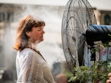 Close-up of a portable misting fan cooling off a smiling person on a sunny patio.