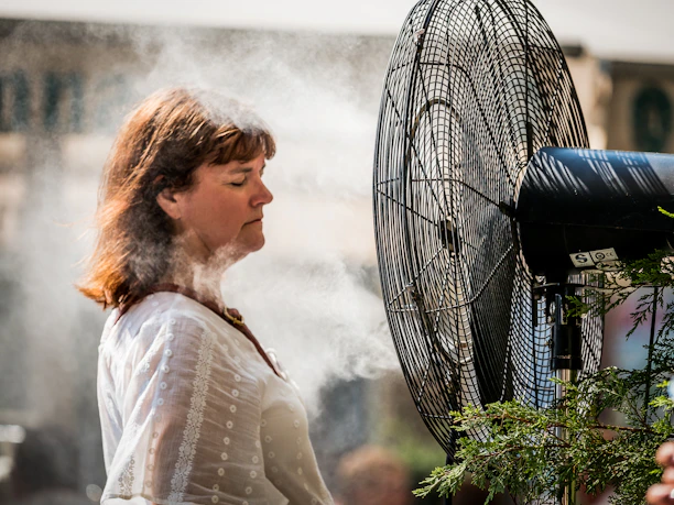 Close-up of a misting fan in action, spraying fine mist on a sunny day.