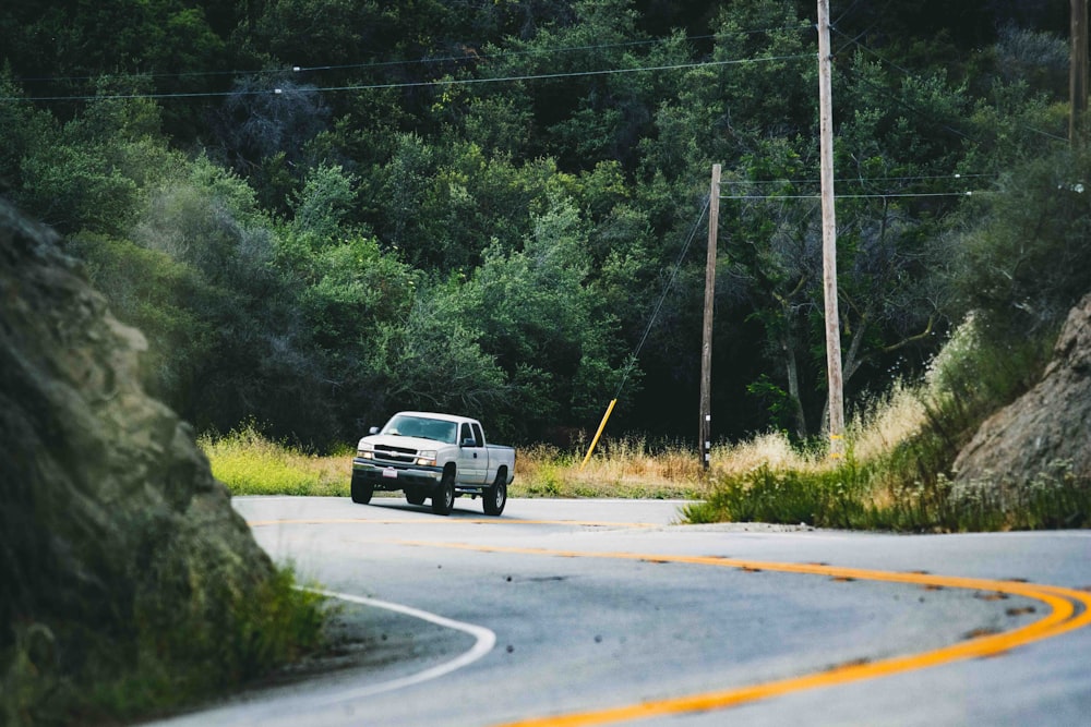 photo of incoming silver pickup truck on road beside hill during daytime