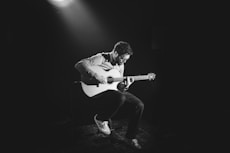 grayscale photo of man playing guitar on stage