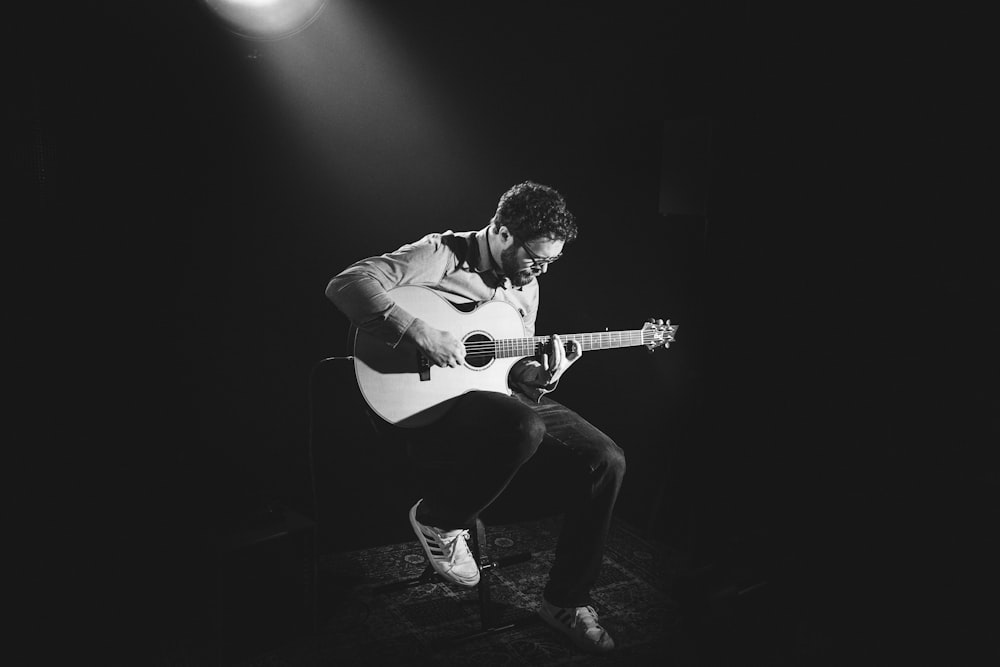 grayscale photo of man playing guitar on stage