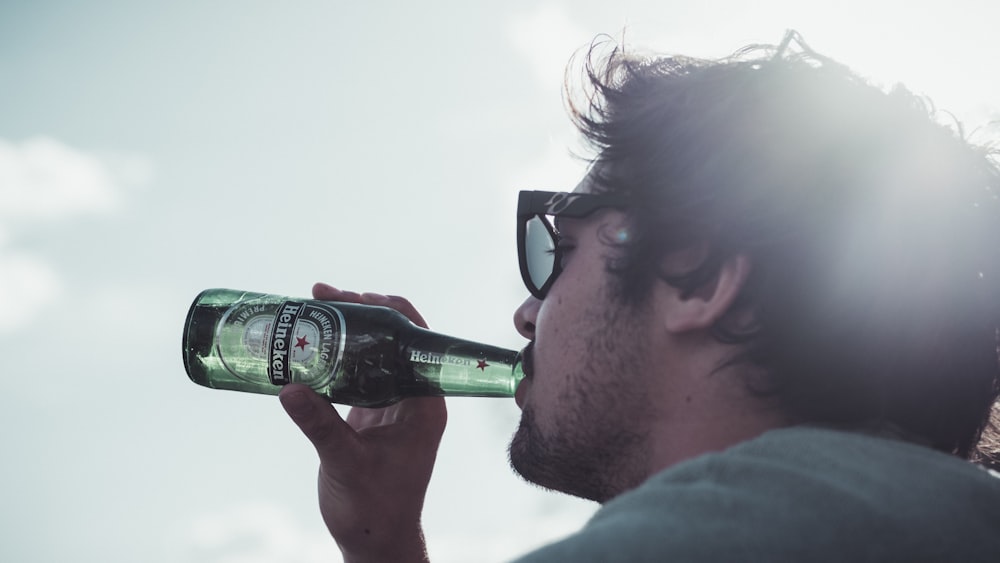 hombre con camisa azul bebiendo una botella de vidrio verde