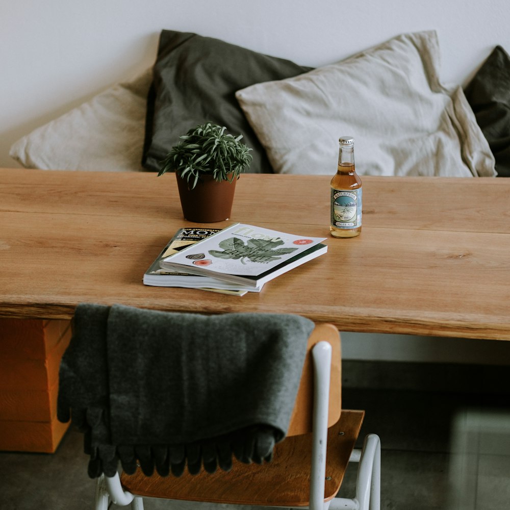 books on table near bottle and leaf plant in pot