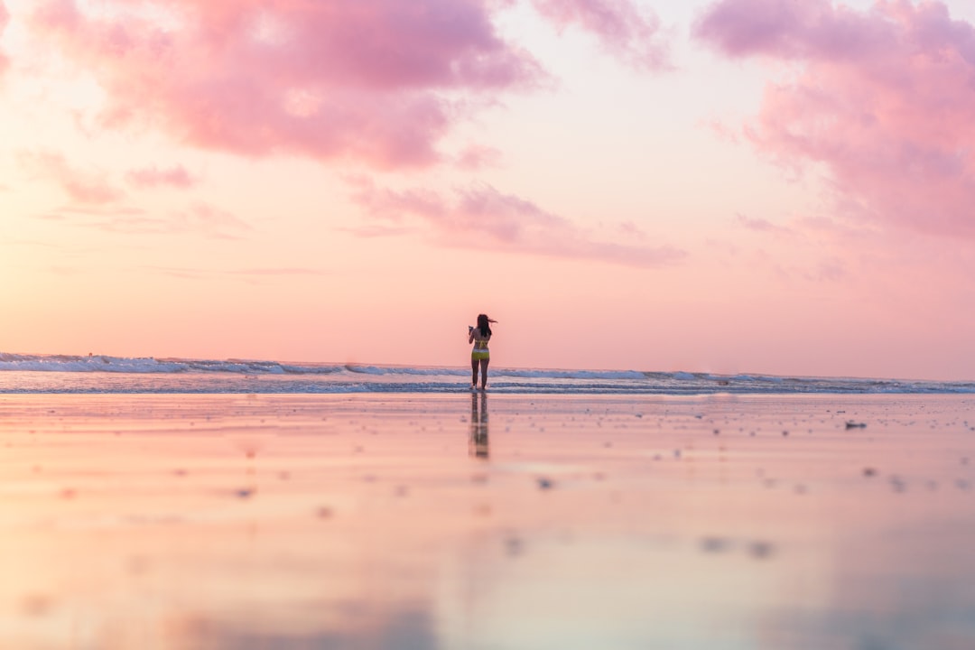 woman standing on seashore in front of body of water, beautiful sunset over bali beach