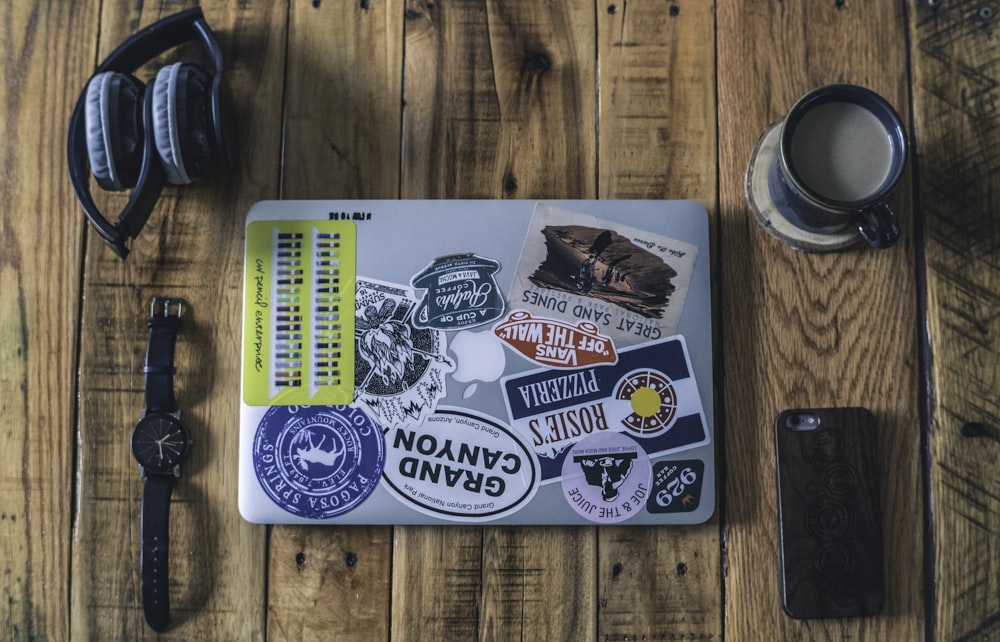 laptop perto do relógio, fones de ouvido, telefone e xícara de café na mesa de madeira marrom