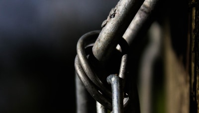 Close-up view of intertwined metal wires, showcasing rough textures and details against a dark background. The focus is on the metal pieces, highlighting their curves and metallic sheen with hints of rust and wear.