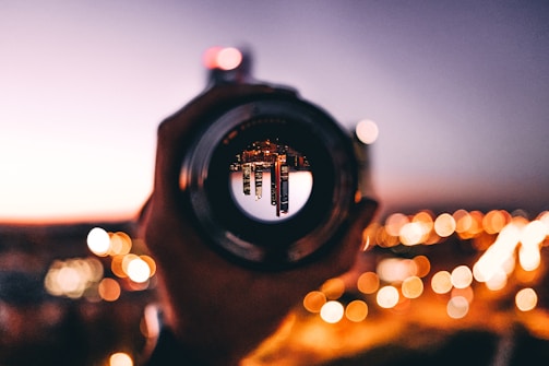 Close-up of a high-end camera lens reflecting a vibrant cityscape at dusk.