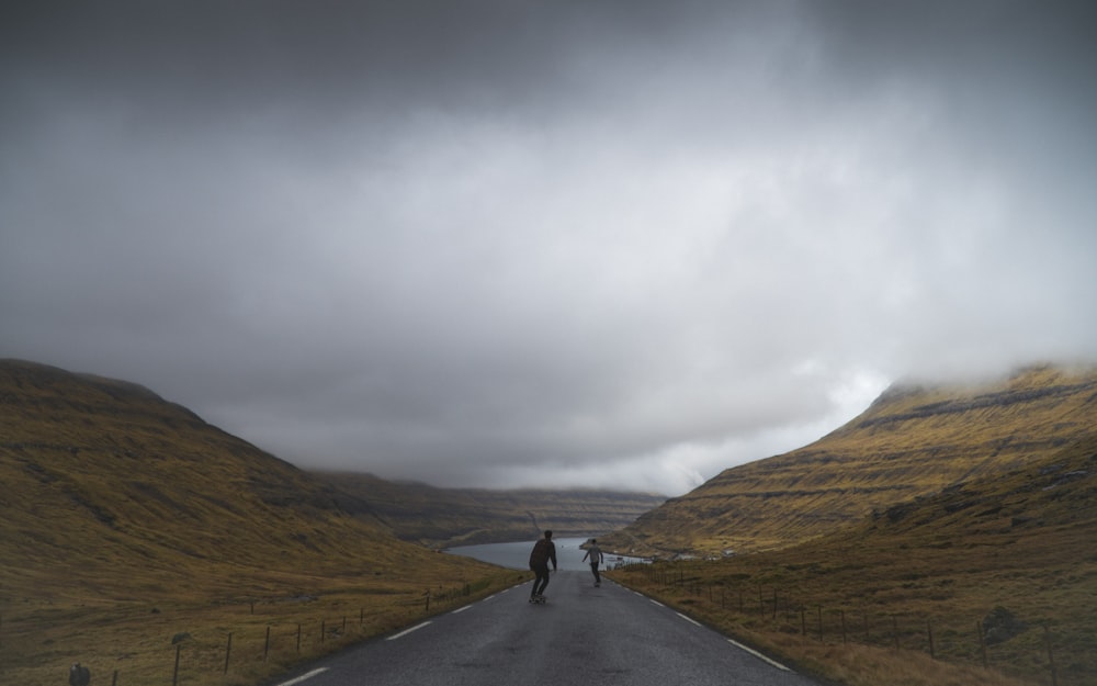 person in black jacket standing on road under cloudy sky