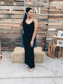 Model wearing a sleek black evening gown standing against a minimalist urban backdrop.