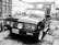 A classic pickup truck with a distinctive front grille and circular headlights parked in an outdoor setting. The vehicle has a Peruvian license plate and is situated against a backdrop of brick walls and assorted household items.