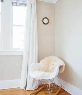 white and brown rocking chair near white painted wall and white window curtain