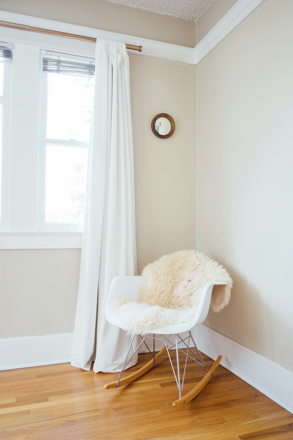 白く塗られた壁と白い窓のカーテンの近くに白と茶色のロッキングチェア