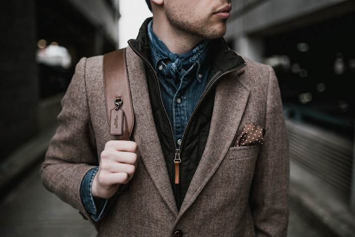 man in brown suit jacket carrying brown backpack