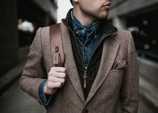 man in brown suit jacket carrying brown backpack