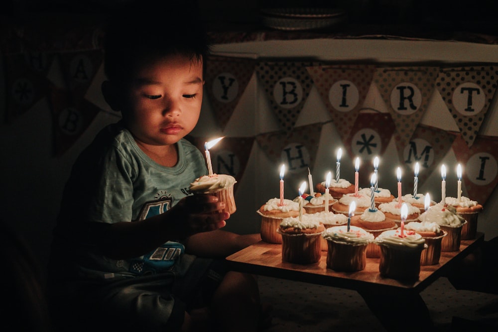 boy holding one of many cupcakes with lit candles