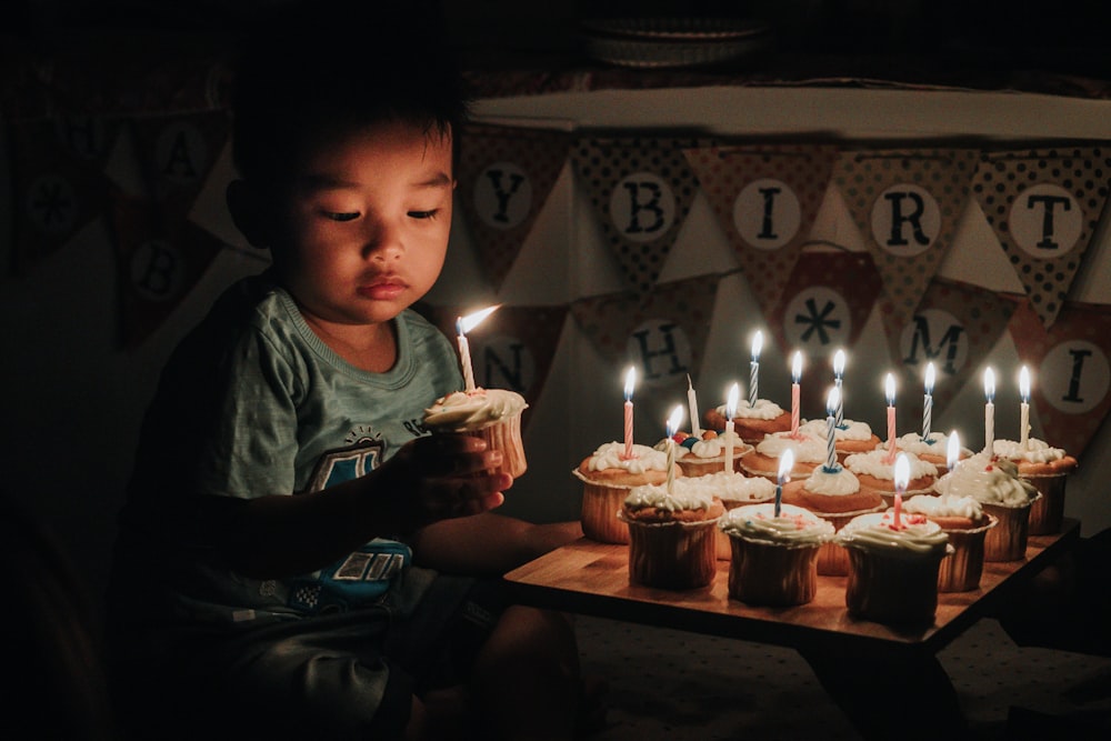 niño sosteniendo uno de los muchos cupcakes con velas encendidas