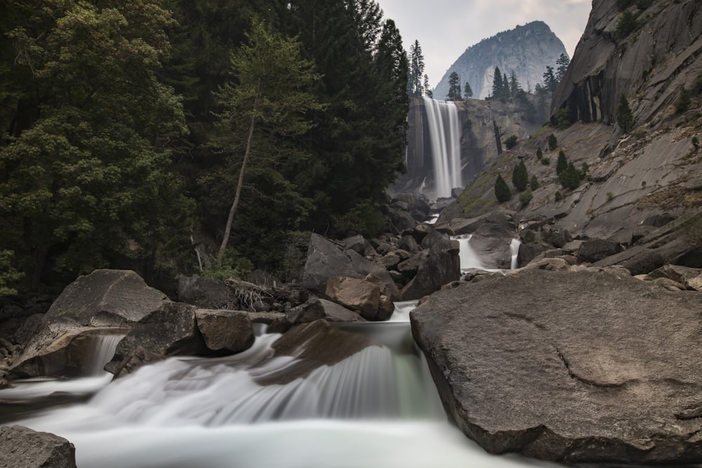 water falls between brown rocks and green trees during daytime