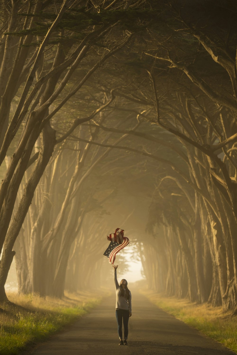 a woman walking down a road holding an american flag