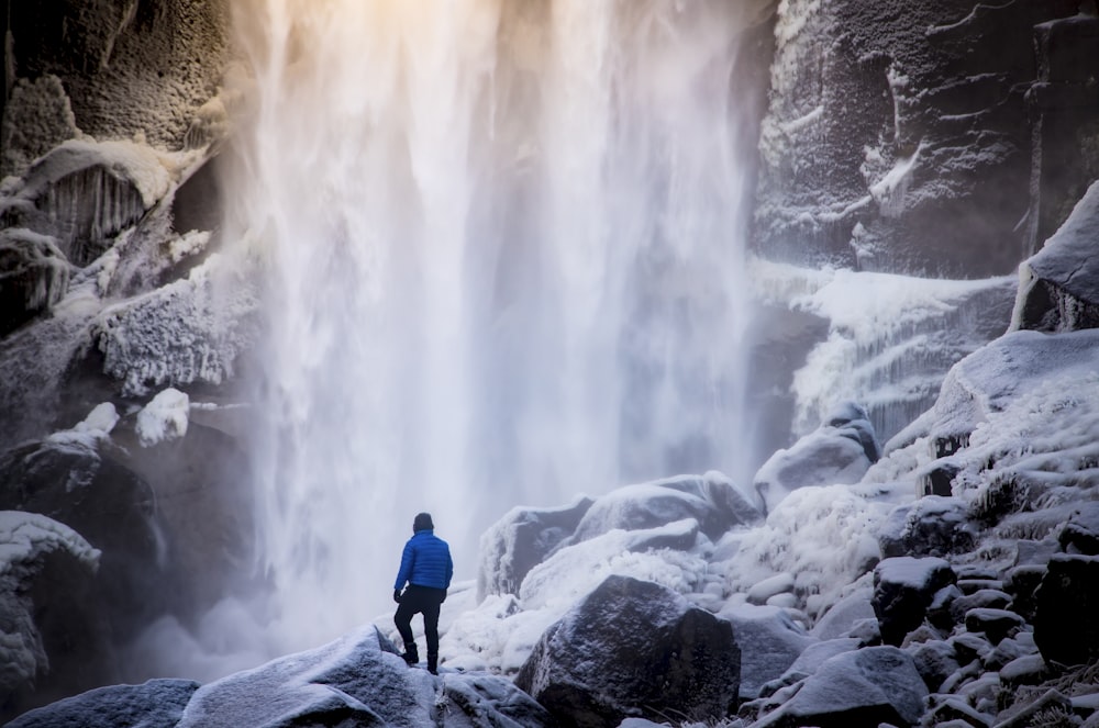 Person, die auf weißem Felsen in der Nähe des Wasserfalls steht
