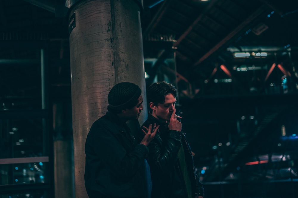 man in black leather jacket holding a cigarette standing beside man talking to him