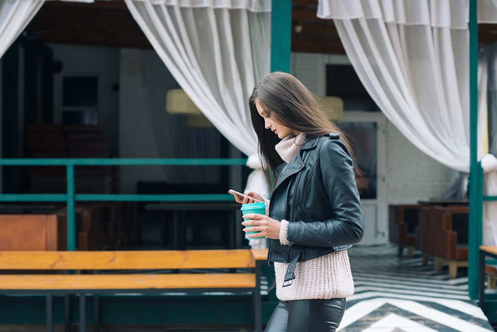 woman using phone while walking near green building